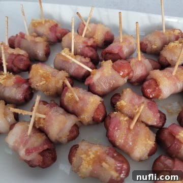 Brown sugar coated bacon wrapped little smokies with toothpicks on a white platter