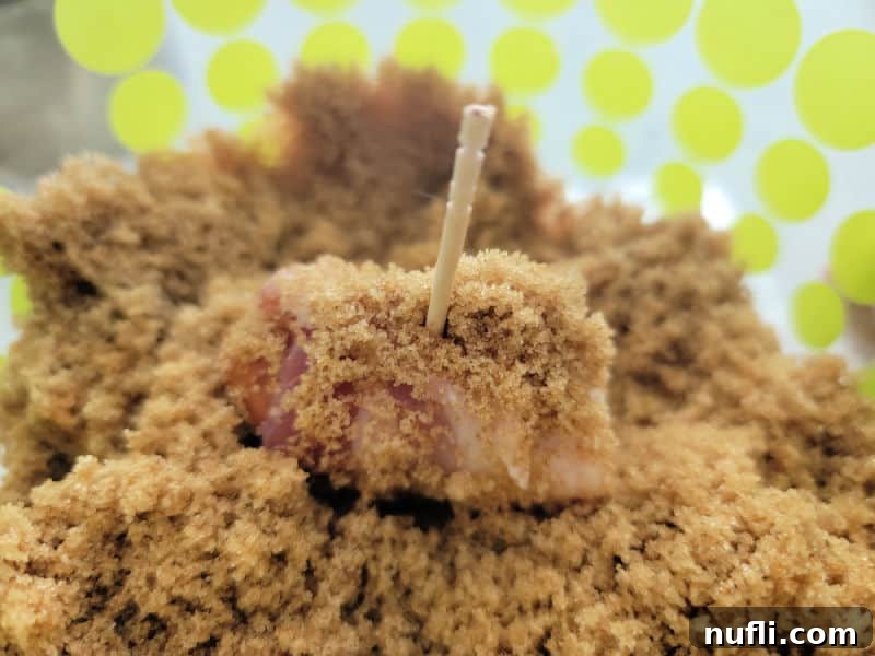 A bacon wrapped lit'l smokie being rolled and coated in a bowl filled with brown sugar.