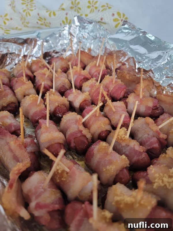 A closer view of the baked brown sugar bacon wrapped little smokies, still in the aluminum foil-lined baking dish, showing their golden crispness.