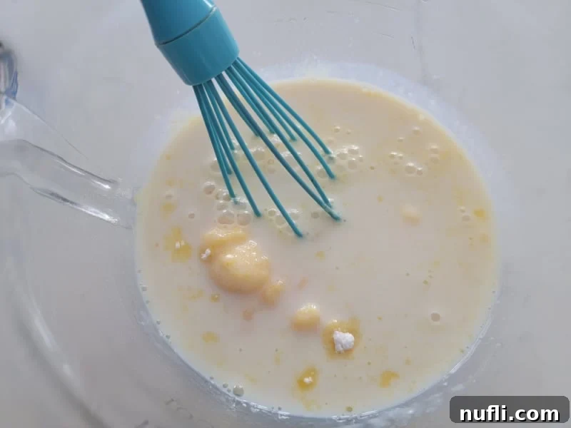Vanilla instant pudding mix being whisked in a clear glass bowl for RumChata Pudding Shots preparation.