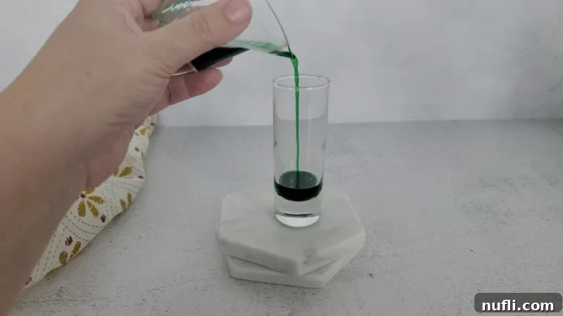 green liquid pouring into a glass shot glass on a white coaster