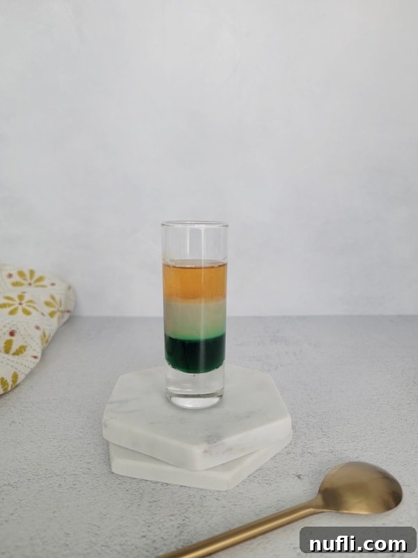 The final layer, Grand Marnier, being added to complete the triple-layered Irish Flag Shot, resting on white coasters.