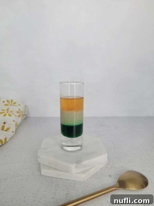 Triple layered shot sitting on white coasters next to a gold spoon and cloth napkin 