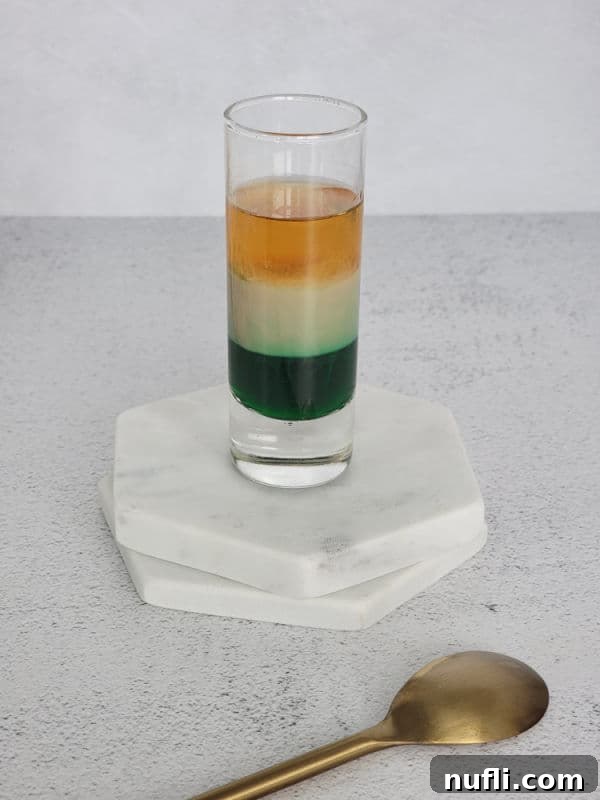 three layered shot sitting on coasters next to a gold spoon 