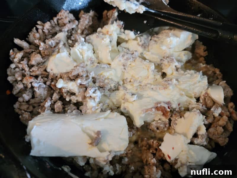 Cream cheese mixing into ground sausage in a cast iron skillet
