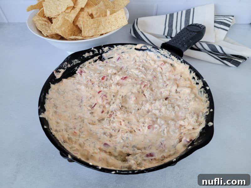 Velveeta dip in a cast iron skillet next to a white bowl of tortilla chips and a cloth napkin