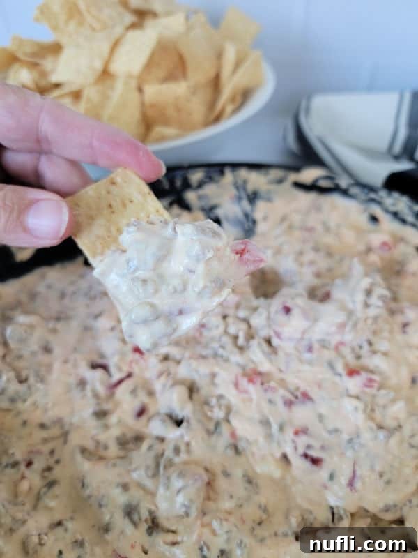 hand dipping a tortilla chip into Velveeta dip next to a bowl of tortilla chips