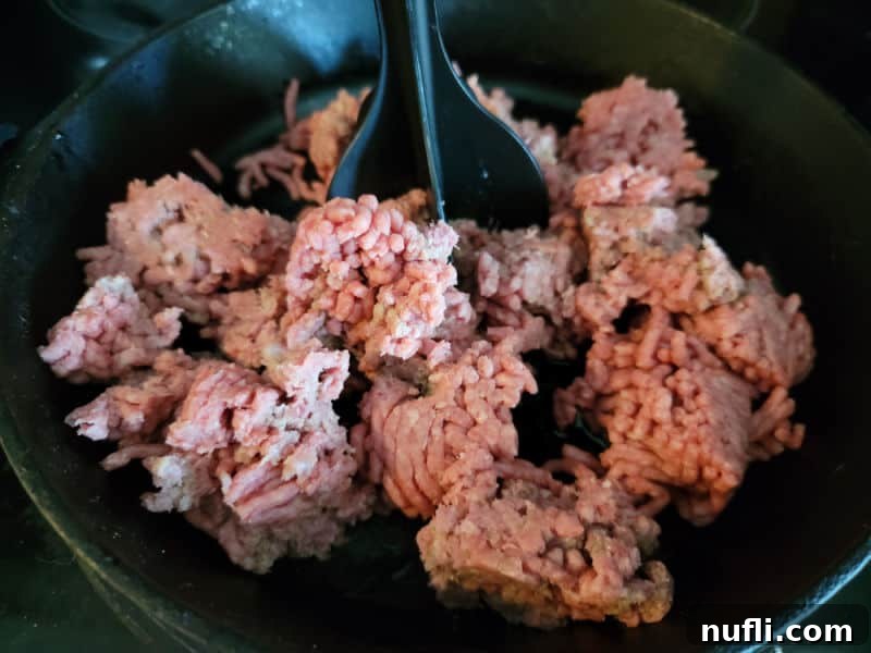 The Easiest 3-Ingredient Velveeta Rotel Ground Beef Dip 4 Ground beef being broken up and browned in a cast iron skillet on a stovetop.