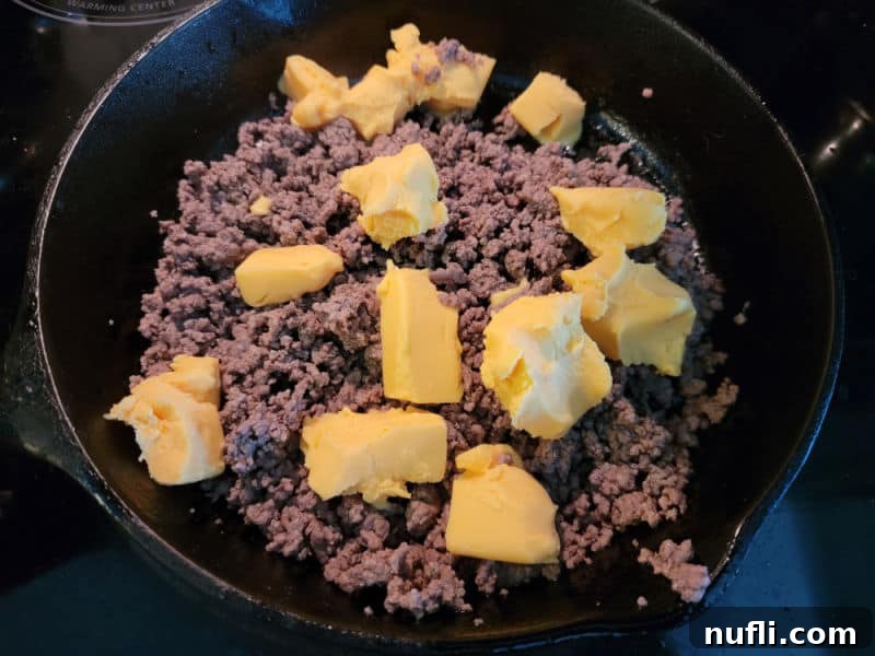 The Easiest 3-Ingredient Velveeta Rotel Ground Beef Dip 5 Cubed Velveeta cheese added to the browned ground beef in a cast iron skillet.