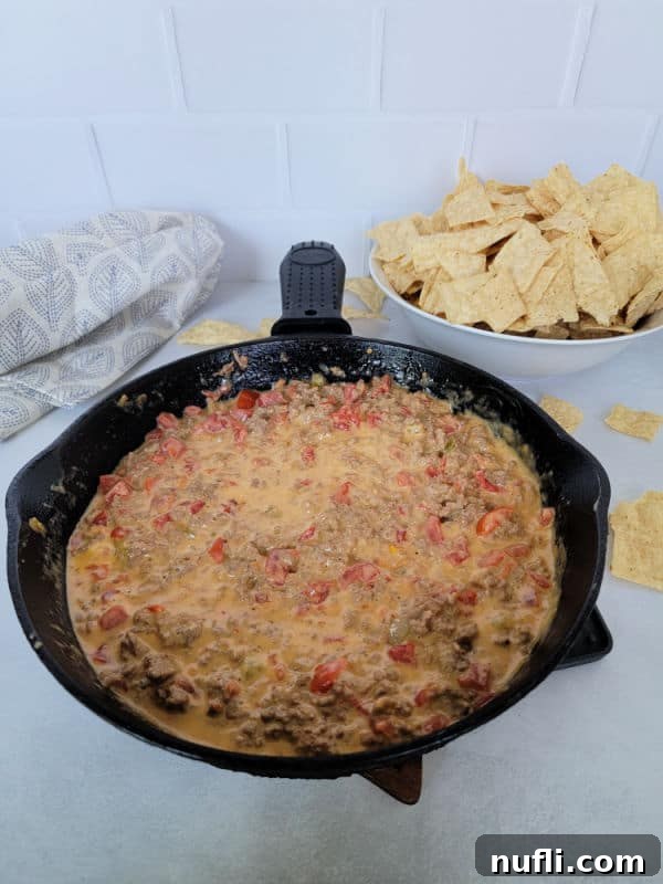The Easiest 3-Ingredient Velveeta Rotel Ground Beef Dip 8 A cast iron skillet filled with Velveeta Rotel Dip, accompanied by a bowl of tortilla chips and a cloth napkin, ready for serving.