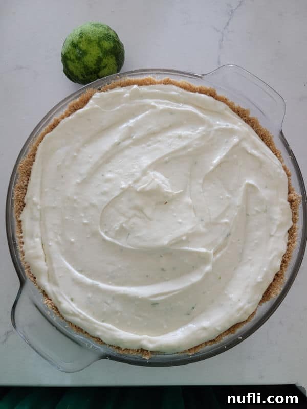 key lime pie in a graham cracker shell in a glass pie plate next to a lime