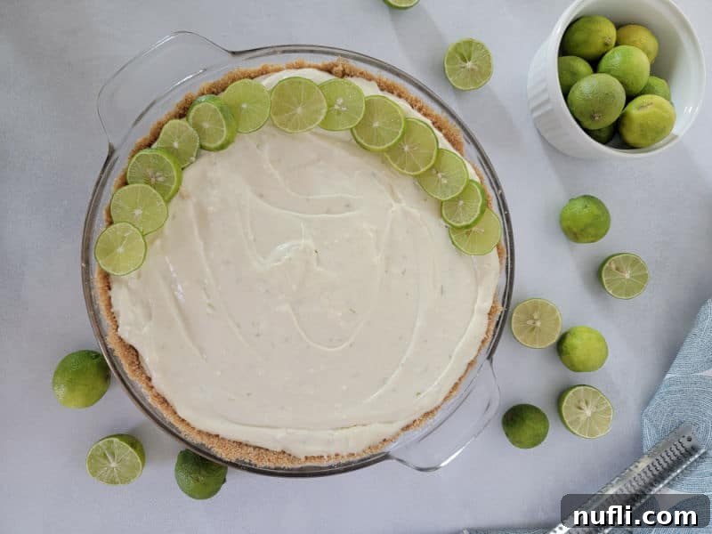 Cool & Creamy Key Lime Pie 5 Key lime circles spread around the edge of a no bake key lime pie in a glass baking dish next to a bowl of limes