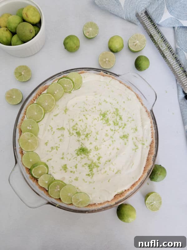Bowl of key limes next to a zester and glass pie dish with key lime pie in it