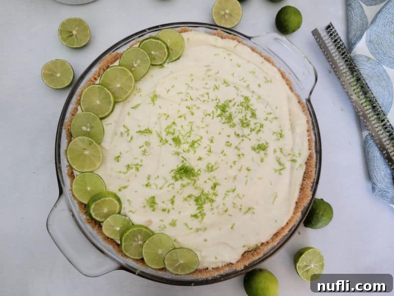 No bake key lime pie in a graham cracker crust in a glass pie dish next to a zester. 
