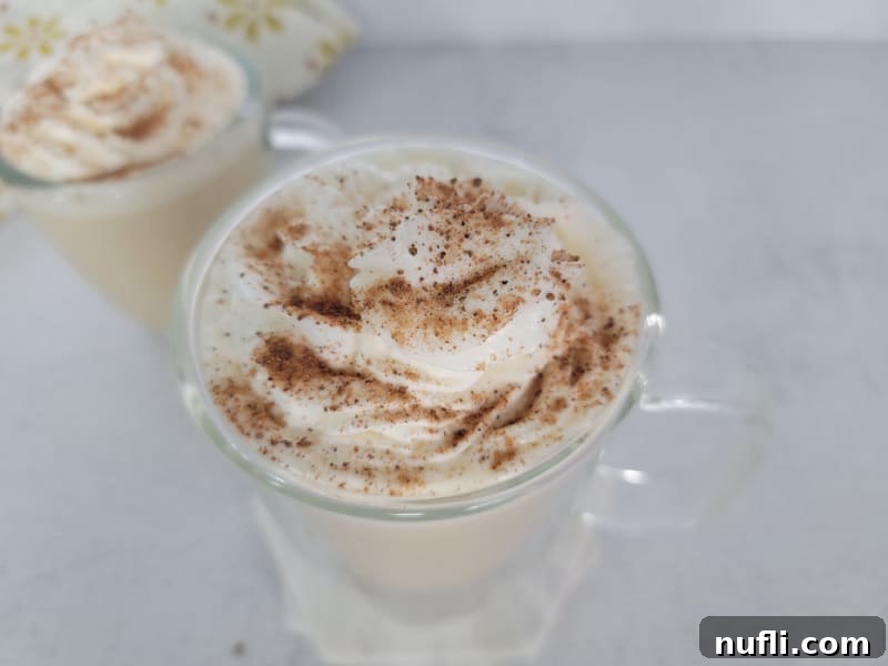 Ground cinnamon and nutmeg on top of whipped cream on an eggnog coffee in a clear glass coffee mug