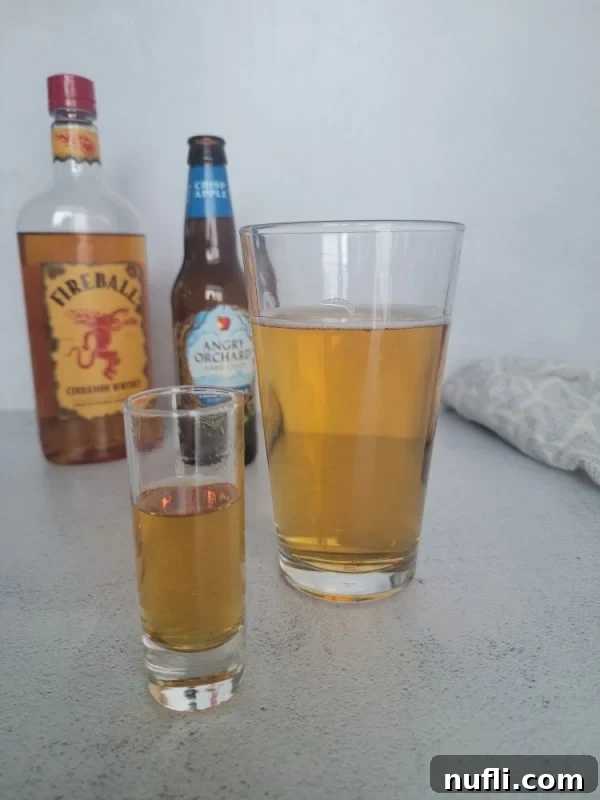 Shot glass next to a glass of beer with a bottle of Fireball and Angry Orchard hard cider in the background