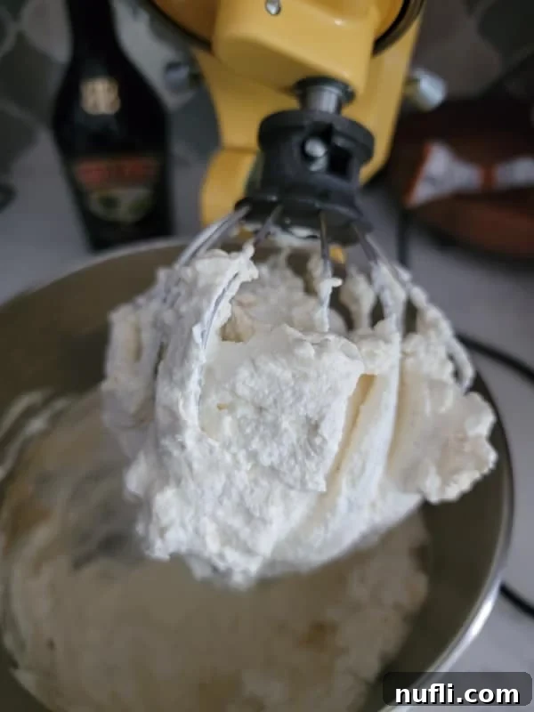 mixer attachment covered in whipping cream above a metal bowl