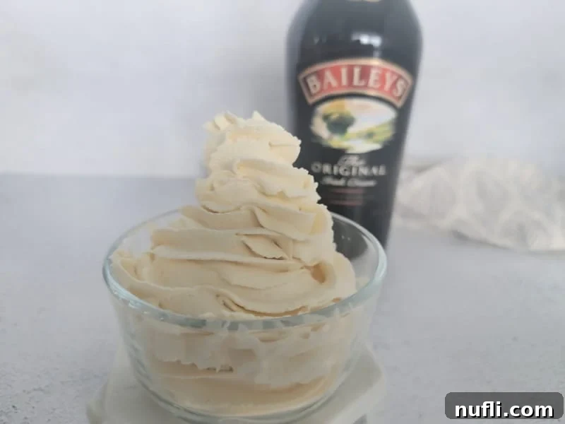 Baileys Whipped cream in a small glass bowl with a bottle of Baileys Irish Cream in the background next to a cloth napkin