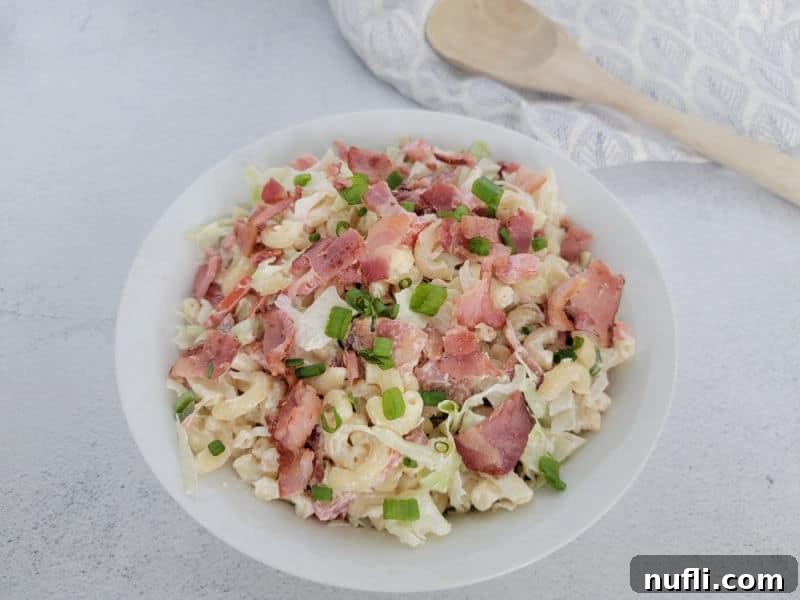 BLT Macaroni Salad in a white bowl next to a wooden spoon and cloth napkin 