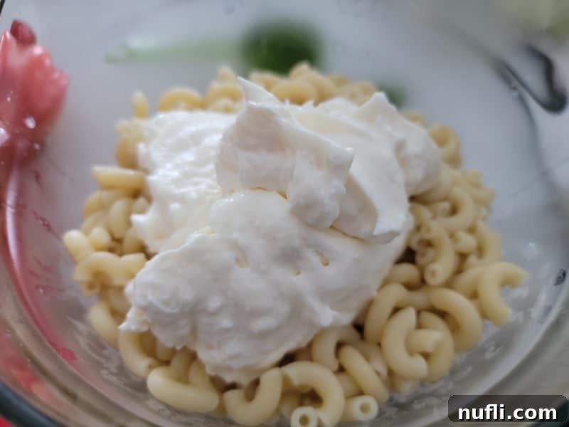 Large dollop of mayo on cooked macaroni in a glass bowl 