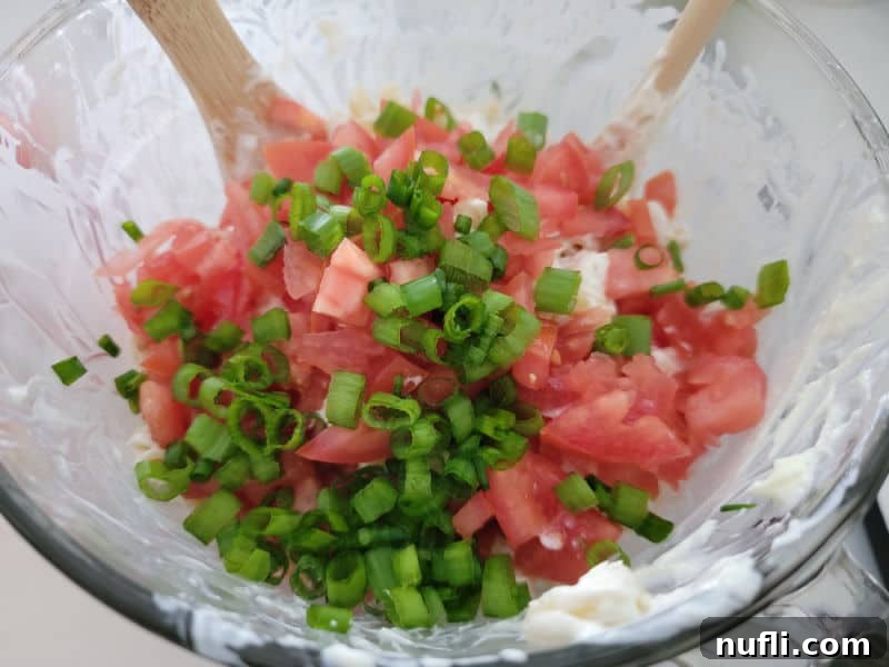 Diced tomatoes and green onions in a glass bowl with a wooden spoon 