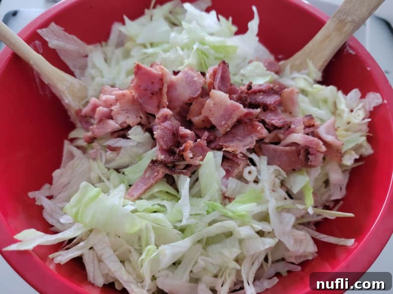 Bacon pieces and lettuce in a red bowl with wooden spoons