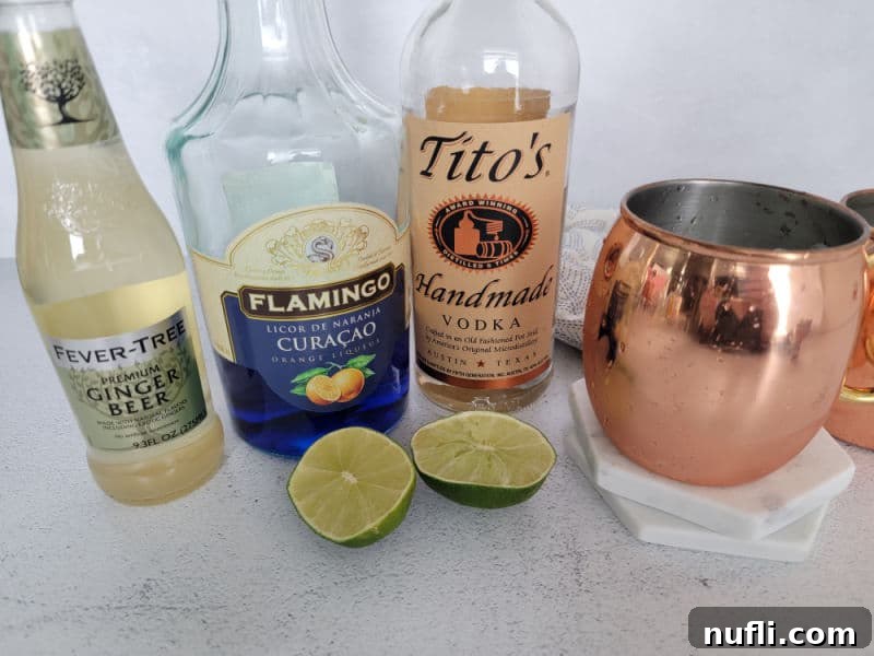 Ginger beer, blue curacao, titos vodka, a cut in half lime, and copper mule mug on a counter