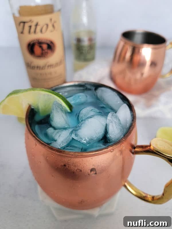 Blue mule in a copper mug next to a bottle of Titos and another copper mule mug