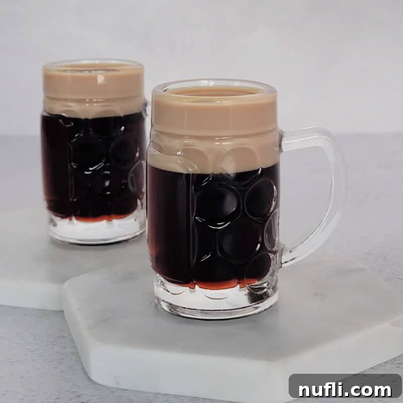 St Patrick's Day Sips & Shots 19 Two perfectly crafted Baby Guinness shots, featuring a dark base topped with a creamy white layer, presented on crisp white coasters, resembling miniature pints of stout.