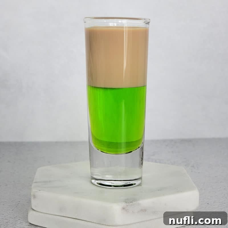 St Patrick's Day Sips & Shots 21 A vibrant layered brown and green cocktail shot, the Irish Frog, beautifully presented on two white coasters, showcasing its distinct colors and creamy texture.
