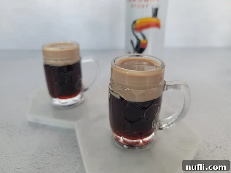 Two Baby Guinness Cocktail Shooters in mini beer glasses on white coasters, showcasing the perfect layers.