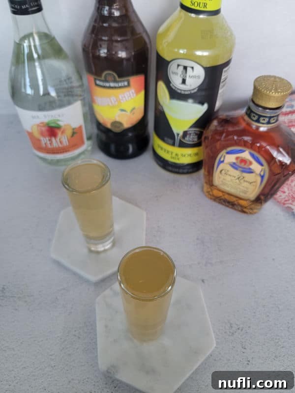 Two filled shot glasses on coasters in front of bottles of liquor