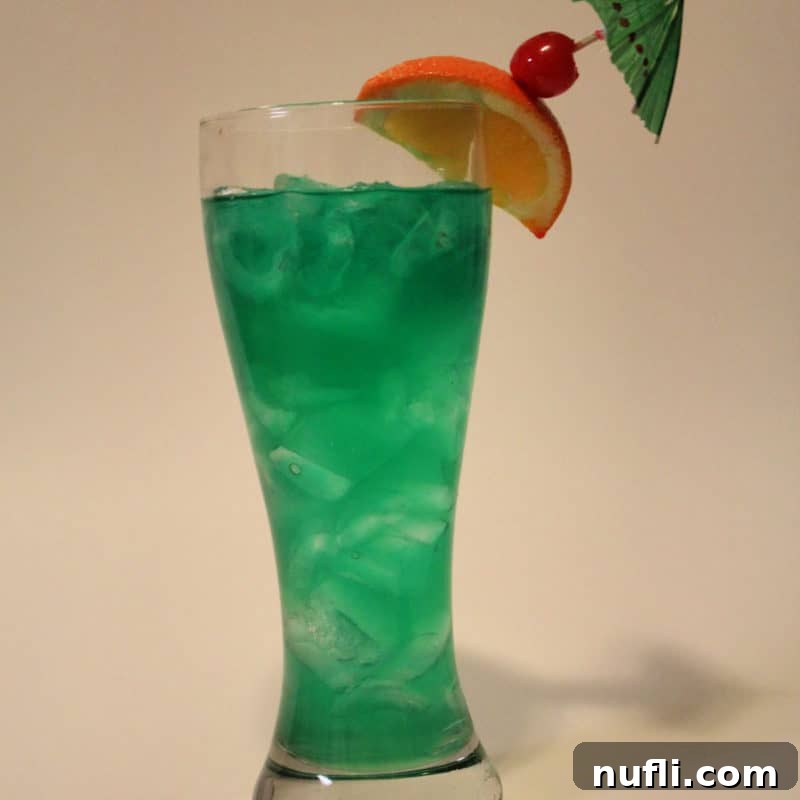 Bright green cocktail in a tall glass with orange slice and cherry garnish