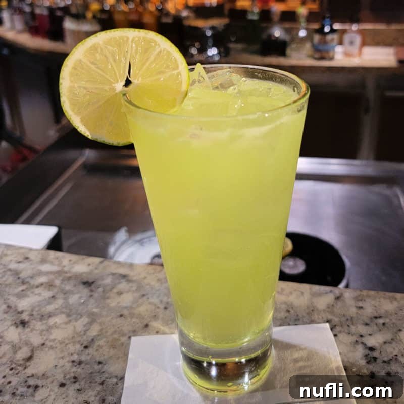yellow green cocktail in a tall glass with lime circle