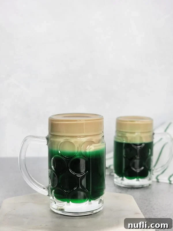 Two perfectly layered Leprechaun Beer Shots in mini beer glasses, showcasing the vibrant green and creamy white layers, ready for St. Patrick's Day celebrations.