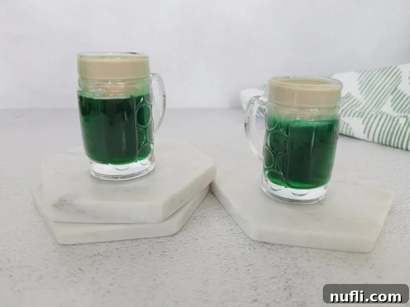 Two green leprechaun beer shots in mini beer glasses on white coasters, showcasing the vibrant green base and creamy white top.