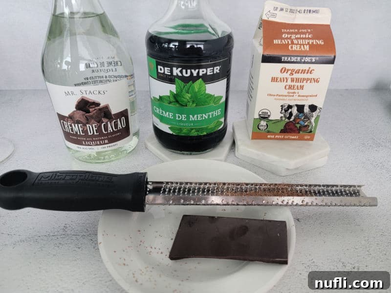Creme De Cacao, Creme de Menthe, Heavy Whipping Cream bottles behind a plate with chocolate on it and a zester