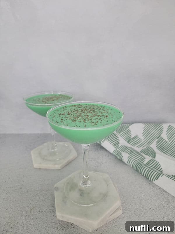 Two green cocktails in coupe glasses on white coasters by a linen towel 