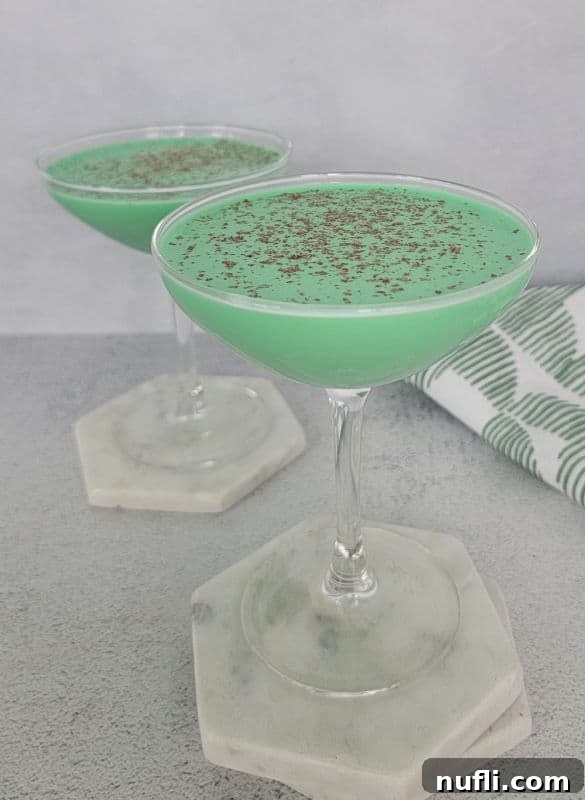 Two green cocktails on white coasters by a green and white cloth napkin