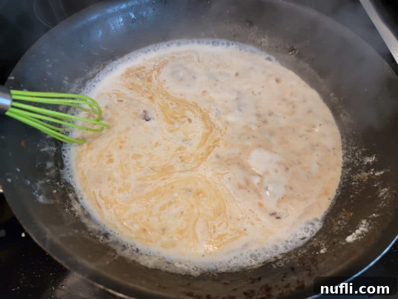 milk adding to bacon grease and flour for bacon gravy in a dark skillet