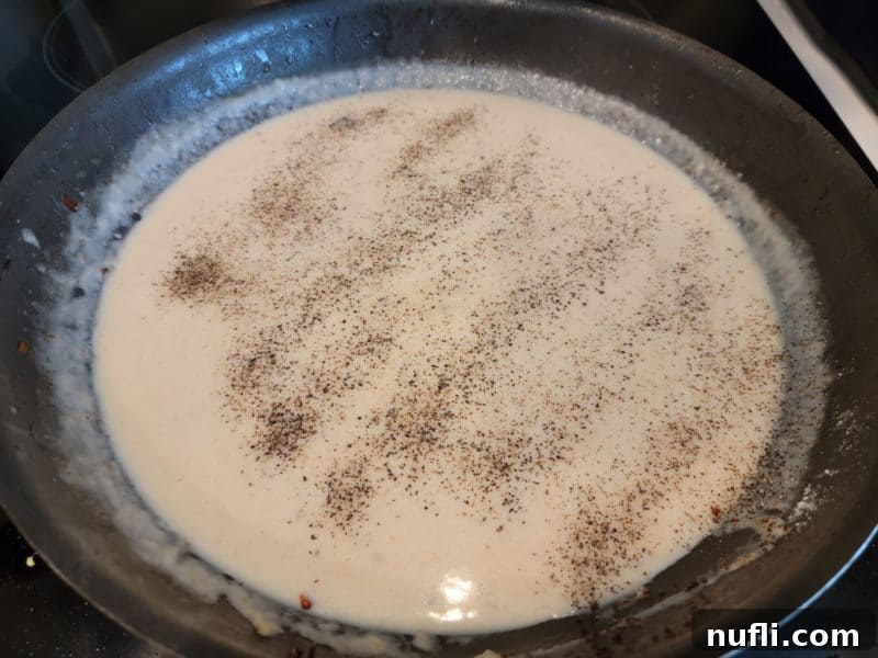  black pepper sprinkled over bacon gravy in a dark skillet