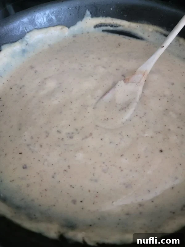 wooden spoon resting in bacon gravy in a dark skillet