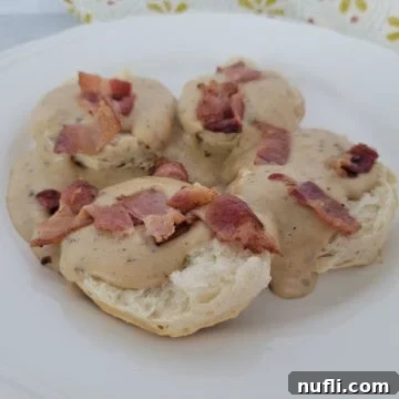 Bacon gravy over biscuits on a white plate with a cloth napkin in the background