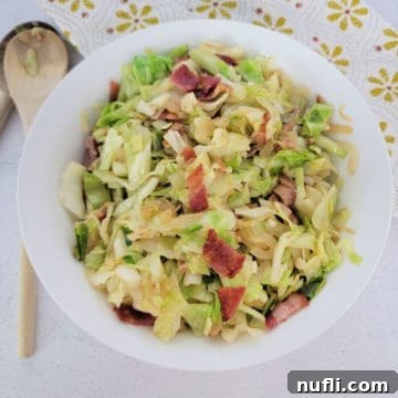 southern fried cabbage with bacon in a white bowl next to a wooden spoon