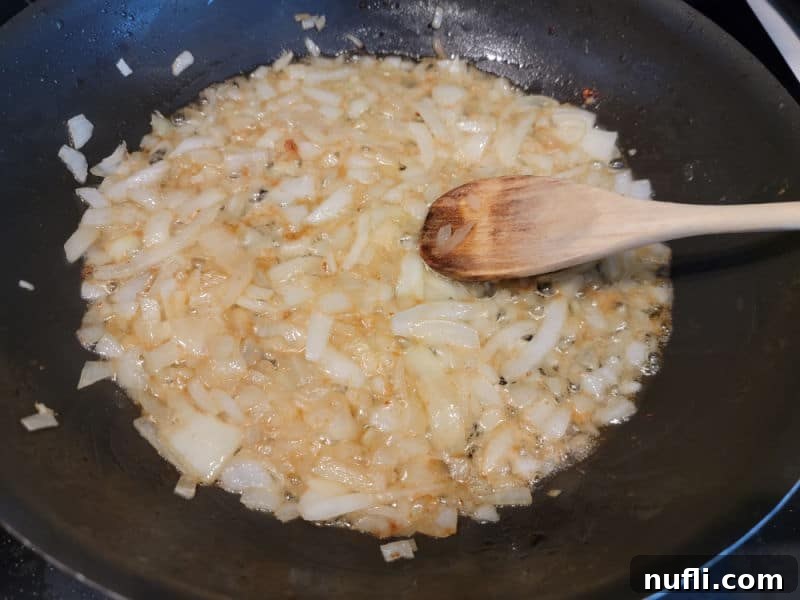 Wooden spoon in onions cooking in bacon grease in a frying pan