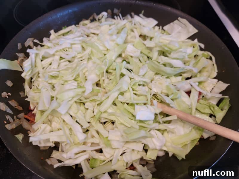 Shredded cabbage in a frying pan with a wooden spoon and bacon