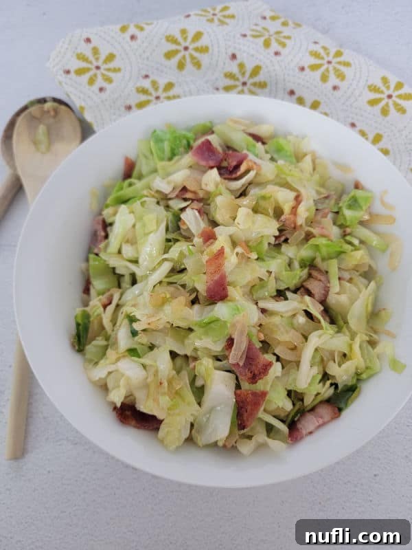 Bacon and shredded cabbage in a white bowl next to a wooden spoon and cloth napkin