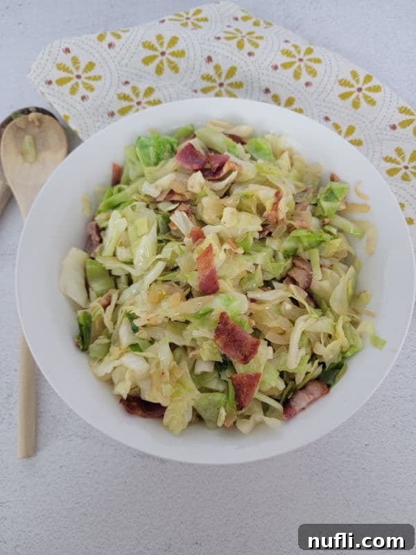 Cabbage and bacon in a white bowl next to wooden spoons and a cloth napkin