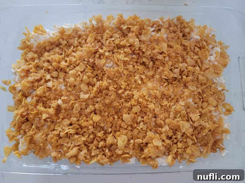 Crushed cornflakes spread over potatoes in a glass baking dish