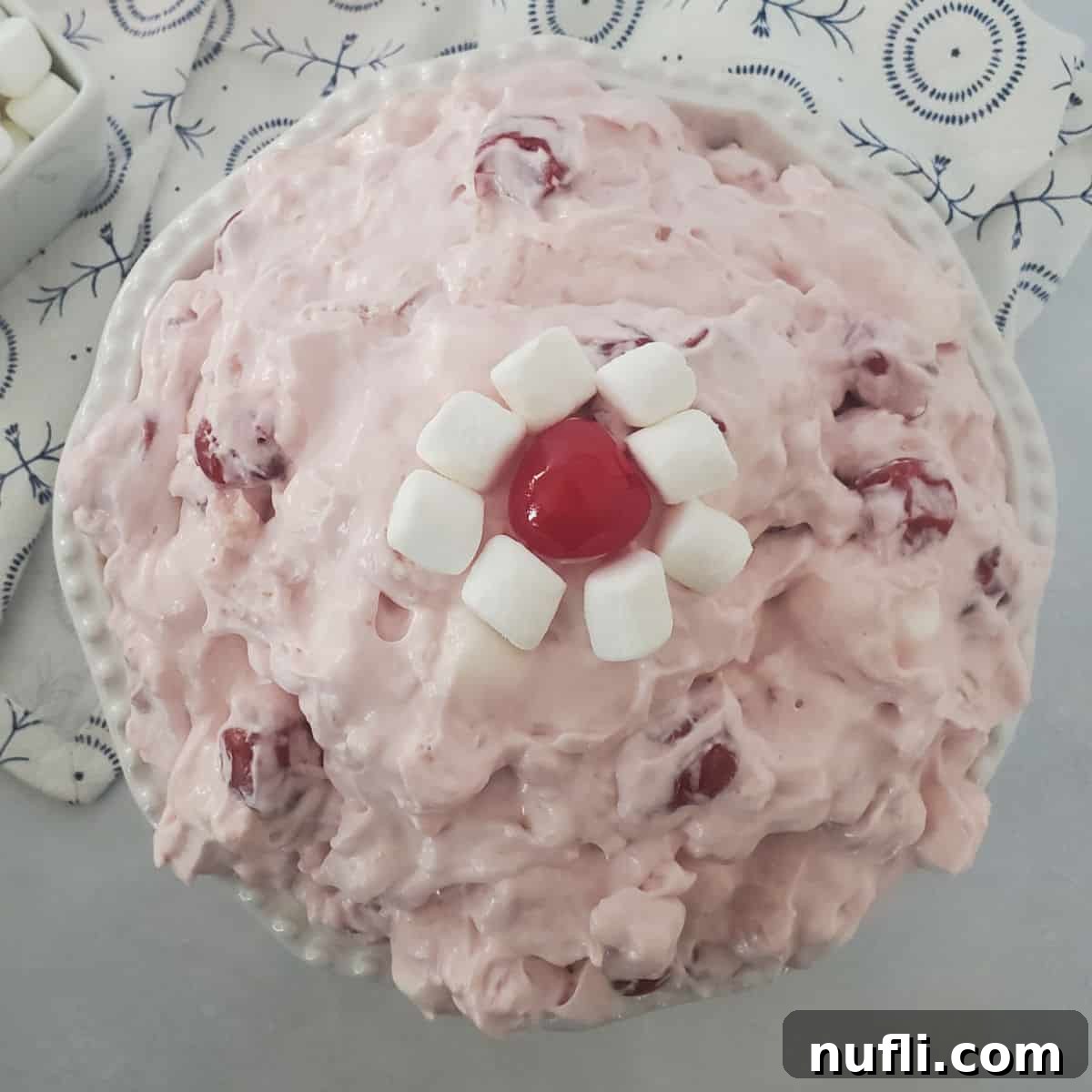 Cherry fluff salad in a white bowl garnished with mini marshmallows and a maraschino cherry